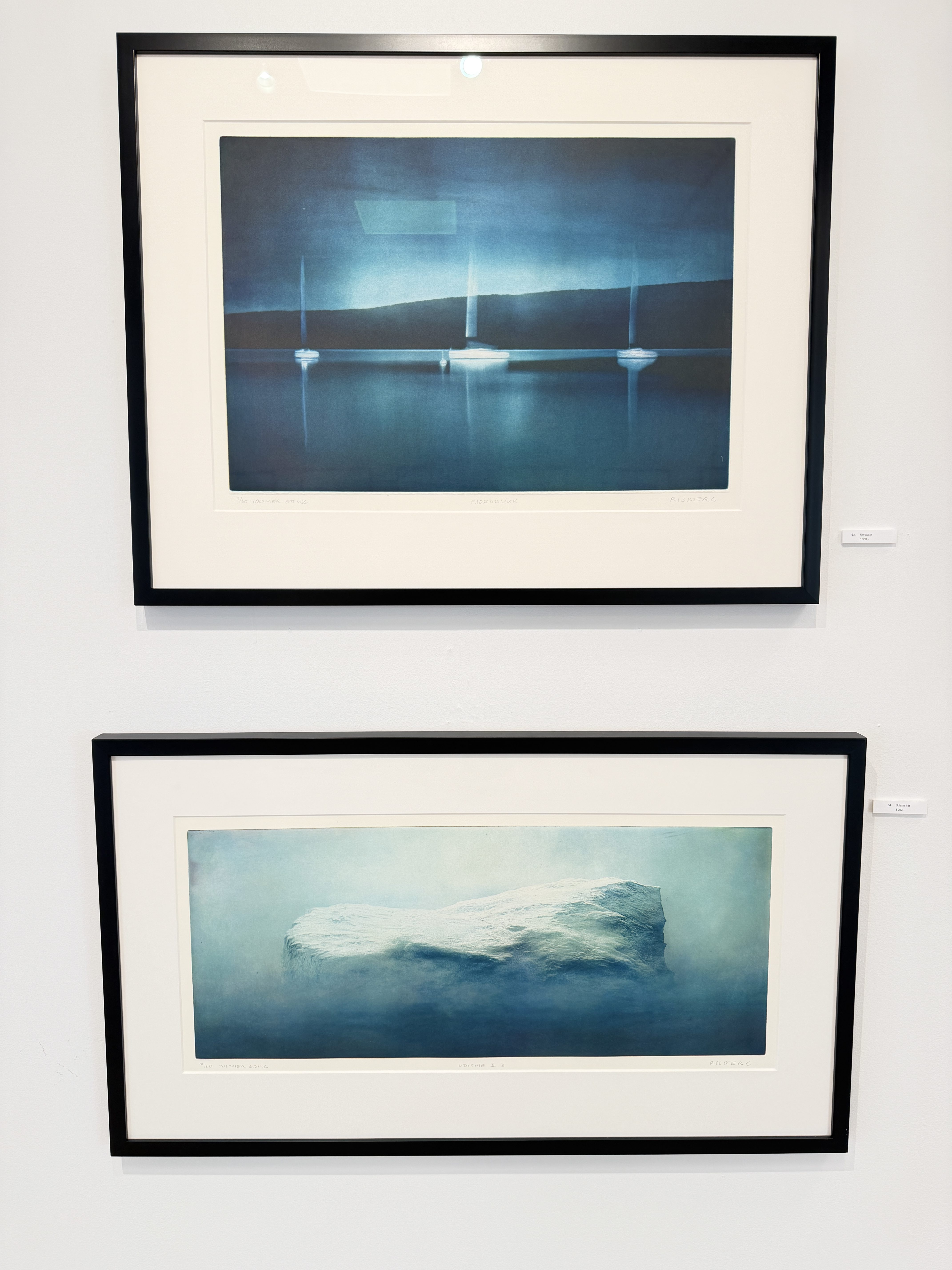 To innrammede blå motiver av seilbåter og et isfjell, fotografert på utstillingsveggen i Galleri BI-Z.
