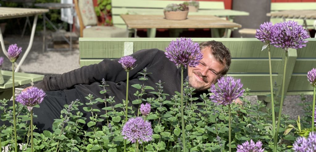 Gartner Emil ligger bak noen lilla blomster