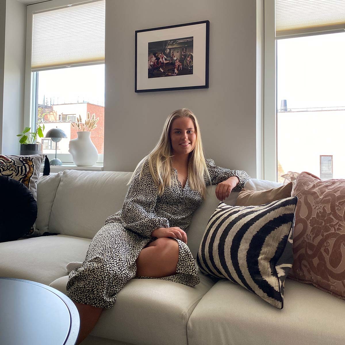 Stine Larsen Strøm jobber for Eske interiør og er her sittende i sin sofa med lekre puter og pledd rundt seg.