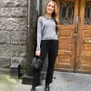 Jente står foran en brun dør med svarte bukser, grå cardigan og en svart håndveske og sølvletter