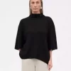 Dame med svart kortermet genser med høy hals kombinert med beige bukse. Damen har grått hår.
