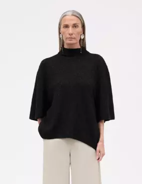 Dame med svart kortermet genser med høy hals kombinert med beige bukse. Damen har grått hår.