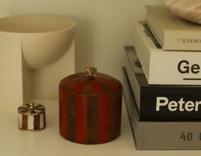 Doing Goods, Piper Cicus Box Large. En stripete rød og brun stor boks og en liten brun og hvit boks med lukk og messing detaljer. Plasser på. en hylle med bøker ved siden av