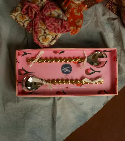 Doing Goods, Holly Heart Salat Server Set. Salatbestikk messing og sølv som ligger i en rosa eske på ett bord